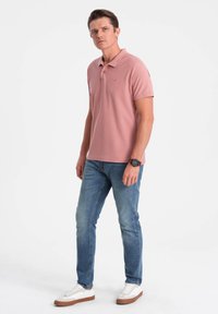 Rosa polo-shirt med korta ärmar, broderad logga, parat med ljusblå jeans och vita sneakers med bruna sulor.