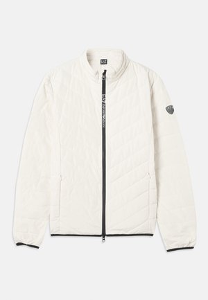 White quilted jacket with a high collar, black zipper, and side pockets. Features a logo patch on the left sleeve. Smooth fabric texture.