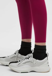 Fuksjowe legginsy w połączeniu z białymi i czarnymi sneakersami z siateczki oraz gładkimi teksturami, okrągłym przodem i gumową podeszwą.