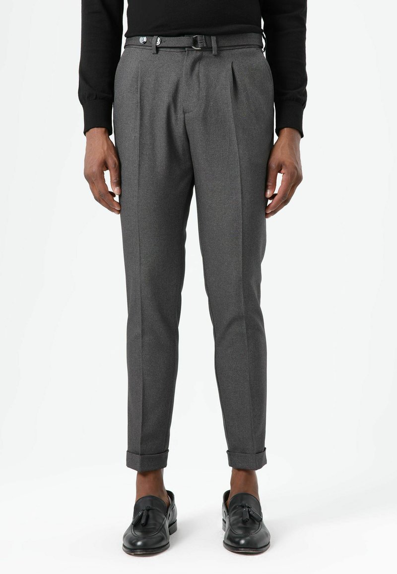 Grau plissierte Anzughose mit schmaler Passform, gekrempelten Säumen und zweiknöpfigem Gürtel-Detail. Hergestellt aus strukturiertem Stoff. Schwarze Loafers getragen.