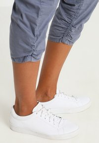 Witte leren sneakers met ronde neuzen en veters, gecombineerd met grijze cropped broeken met geplooide details aan de zoom.