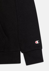 Czarna bluza z materiału z ribbowymi mankietami, z małym haftowanym logo w czerwonym i białym kolorze na lewym rękawie. Klasyczny wzór.