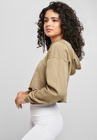 Īss kapucētkrekls bēšā audumā ar platajām piedurknēm, kombinēts ar augstu jostasvietu baltiem legingiem. Gluda tekstūra un brīvs piegriezums.