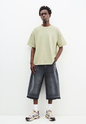 Overdimensioneret lysegrøn bomulds t-shirt, mørkegrå denim culottes med flosset kant, og mønstrede sneakers. Hvite crew-sokker fuldender looket.