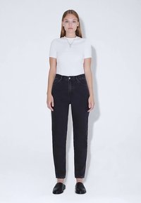 Černé džíny s vysokým pasem a rovnými nohavicemi, vybavené předními kapsami a zapínáním na knoflík. Kombinovány s bílým přiléhavým tričkem s krátkými rukávy.