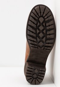 Braune Lederschuhe mit einer strukturierten Gummisohle, die ein gemustertes Profil für besseren Halt aufweist. Die Seite zeigt eine glatte Oberfläche mit feinen Nähten.