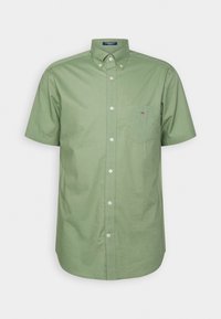 Chemise à manches courtes vert olive à boutons, avec poche et col, présentée sur un fond blanc uni.