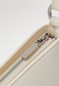 Interno di una borsa in pelle beige con una cerniera argentata, dotata di un cursore inciso con "HUGO" e una consistenza liscia.
