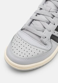 Gray leather sneaker with perforated toe, flat gray laces, black stripes, and a textured white rubber sole.