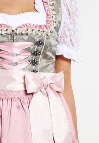 Lederhosen dress features a green bodice with heart patterns, pink ribbons, silver flower accents, and a pink polka-dot skirt with a bow.