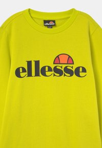 Felpa verde lime con scollatura rotonda. Presenta un grande logo nero con la scritta "ellesse" e un design a mezzaluna arancione sopra di esso.