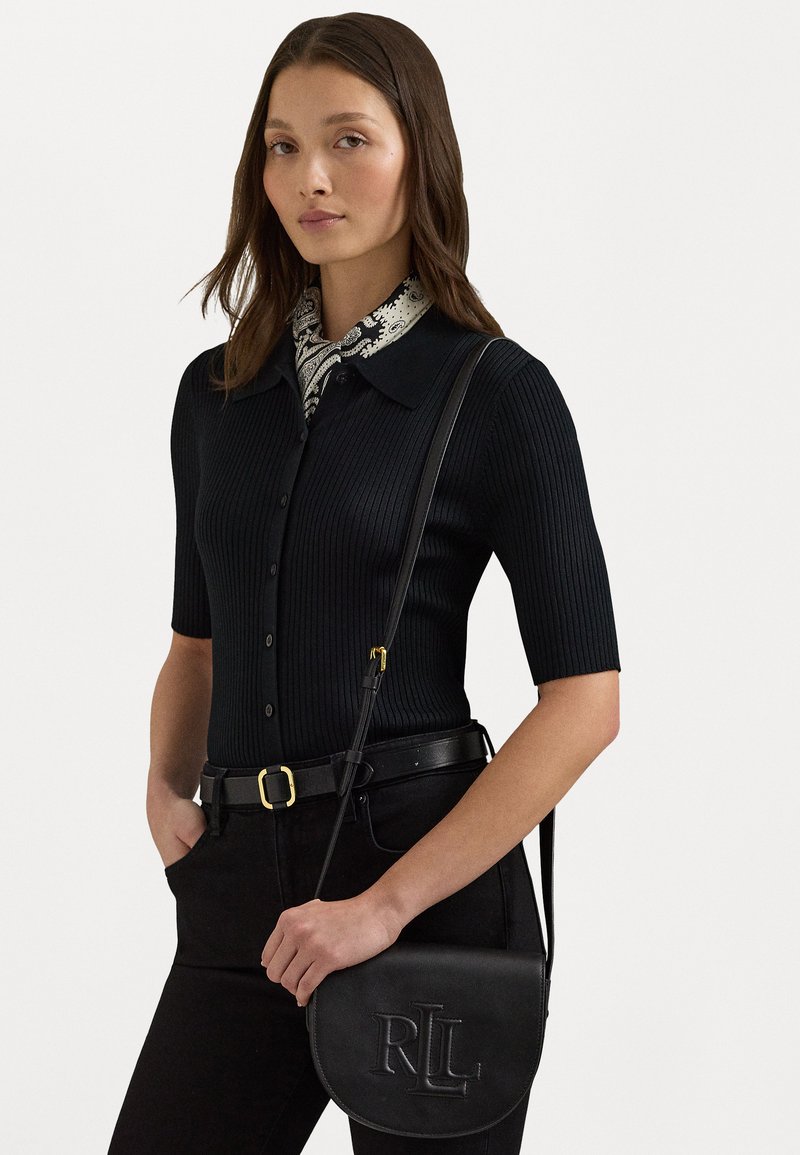 Black ribbed knit top with short sleeves and a collar, paired with a patterned scarf. Holding a black leather crossbody bag with embossed logo.