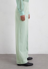 Lichtgroene wijde broek gemaakt van een glad materiaal, met een vlakke voorkant en zijzakken, gecombineerd met zwarte hoge laarzen.
