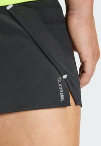 Close-up of a person's thigh wearing black athletic shorts with "CLIMACOOL" text on the hem and a small side slit.
