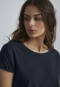 Navyblaue Baumwoll-T-Shirt mit rundem Halsausschnitt und kurzen, aufgerollten Ärmeln. Weicher Stoff mit glatter Textur, minimalistischem Design und ohne Muster.