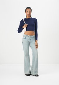 Navy long-sleeve crop top, light blue flared jeans, and black shoes. Model carries a small pink bag, featuring a smooth fabric texture.