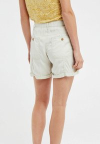 Pantaloni corti chiari con una vestibilità rilassata, caratterizzati da tasche posteriori e risvolti. Realizzati in tessuto morbido e texture, con una vita elastica.