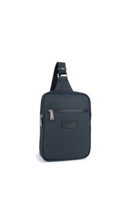 Borsa a tracolla blu scuro con finitura in nylon liscia, dotata di una tasca frontale con zip, cinghia regolabile e una placca con logo. Dimensioni: compatta e rettangolare.