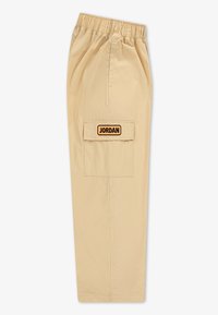 Beige cargo-bukser med elastisk talje, der har en stor baglomme og et sort og orange "JORDAN" patch. Glat tekstureret overflade.