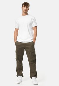 White short-sleeve t-shirt paired with olive green cargo pants featuring side pockets, completed with white sneakers. Simple, casual outfit.
