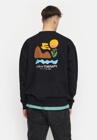 Zwart sweatshirt met kleurrijk grafisch ontwerp: een vogel, berg, zon, bloem en watermotief. Losse pasvorm met geribde manchetten en zoom.