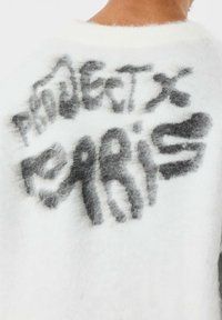 Witte, fluffy trui met een zwarte grafische print met de tekst "PRODGET X PARIS" op de achterkant. Zachte textuur met een ronde halslijn.