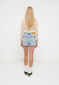 Csipkés, hosszú ujjú felső nyitott hátrésszel, világoskék farmer rövidnadrággal párosítva. A rövidnadrág derékrészén folt található, és kopott szegélyek díszítik.