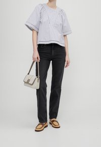 Personne portant un chemisier à manches courtes rayé, un jean noir, des mocassins tissés marron, tenant un petit sac à main beige avec une bandoulière.