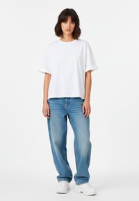 T-shirt bianca oversize a maniche corte abbinata a jeans azzurri morbidi e scarpe da ginnastica bianche. Design semplice, texture liscia e taglio classico.