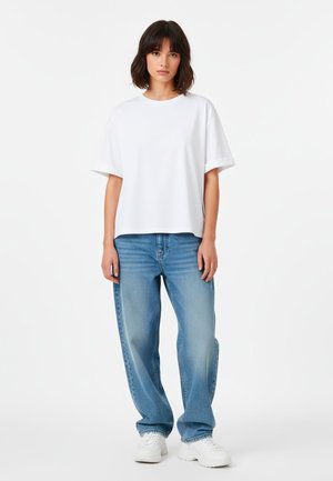 Witte oversized T-shirt met korte mouwen, gecombineerd met lichtblauwe, loszittende jeans en witte sneakers. Eenvoudig ontwerp, gladde textuur en klassieke snit.