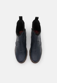 Bottines en cuir bleu foncé avec des zips latéraux, doublure noire texturée, et semelles en caoutchouc marron. Deux languettes de tirage en haut de la cheville.
