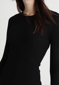 Maglietta nera a maniche lunghe a coste con una silhouette aderente. Presenta un collo rotondo e un tessuto testurizzato per un tocco di dettaglio in più.