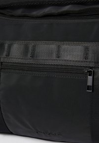 Černá látková taška s texturovaným povrchem, kapsou na zip a detailem popruhu. Hladký povrch a elegantní design s minimálními akcenty.