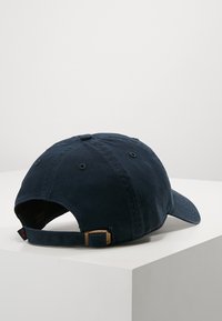 Navy cotton baseball cap with a curved brim, adjustable strap, and subtle texture. Features a logo tag on the side and stitching details.