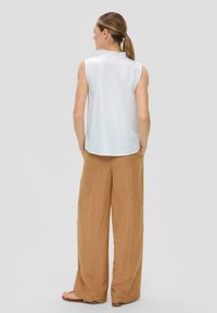Biała bezrękawnikowa bluzka z falbaną przy dekolcie, w połączeniu z szerokimi brązowymi spodniami. Gładki materiał o luźnym kroju.