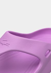 Κοντινό πλάνο μοβ σαγιονάρας από καουτσούκ με λογότυπο κροκόδειλου στο πλαϊνό λουράκι.