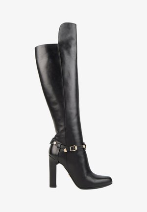 Botte en cuir noire hauteur genou avec talon bloc haut et sangle décorative avec boucle dorée autour de la cheville.