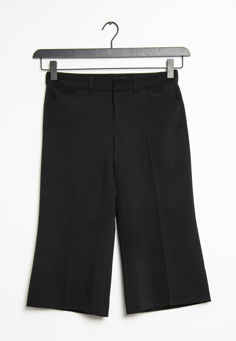 Pantalon noir large longueur genou avec passants de ceinture et poches avant accroché sur un cintre noir sur fond blanc.