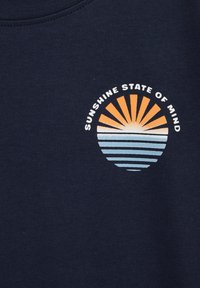 Granatowa koszulka z okrągłą grafiką przedstawiającą wschodzące słońce w odcieniach pomarańczowym i niebieskim, z napisem "SUNSHINE STATE OF MIND" powyżej.
