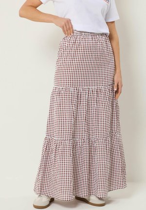 Femme portant une jupe longue à volants vichy marron et blanc avec taille élastique, associée à des baskets blanches et un t-shirt blanc.