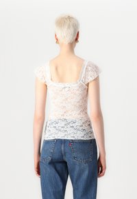 Hvit bluse i blonder med korte, lette ermer, med blomsterdesign og en litt tettsittende passform, brukt med høy midje blå jeans.