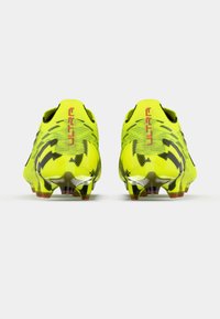 Botas de fútbol de color amarillo brillante con detalles en negro, diseño aerodinámico y superficie texturizada. Presentan una marca distintiva "ULTRA" en el talón.