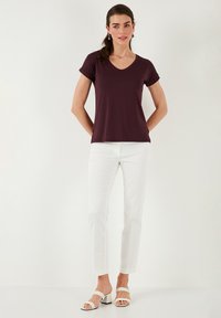 Burgundské tričko s výstřihem do V a krátkým rukávem, doplněné bílými slim-fit kalhotami a bílými sandály na blokovém podpatku, představené na neutrálním pozadí.