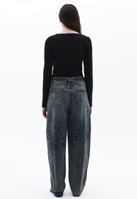 Camiseta negra de manga larga combinada con unos vaqueros holgados de denim azul deslavado. Incluye bolsillos traseros y costuras visibles. Diseño simple y ajustado.