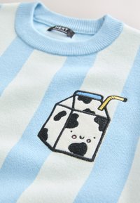 Vêtement rayé bleu et blanc avec un motif brodé d'une boîte de lait dessin animé à taches noires, un visage souriant et une paille jaune près du col.