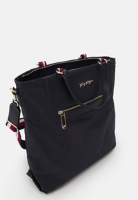 Borsa a spalla in nylon blu con accessori dorati, scomparto principale con zip e tasca frontale. I dettagli includono strisce rosse e bianche sulle cinghie.