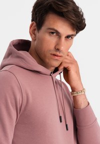 Felpa con cappuccio rosa chiaro, dotata di lacci con estremità nere. Tessuto morbido, design aderente e polsini a costine. Abbigliamento casual.