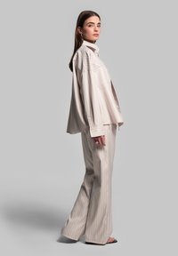 Lichtbeige gestreepte shirt en bijpassende wijde broek, beide gemaakt van gladde stof. Ontspannen pasvorm met verlaagde schouders en een kraag.
