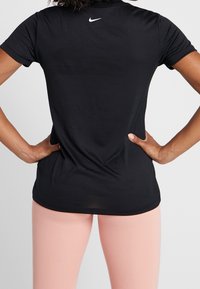 Svart kortärmad sportt-shirt med rund halsringning, med en liten vit Nike-logotyp på baksidan. Bärs med ljusrosa tights.