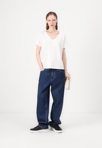 White short-sleeve V-neck t-shirt paired with loose-fitting dark blue denim jeans, black lace-up sneakers, and a small beige handbag.